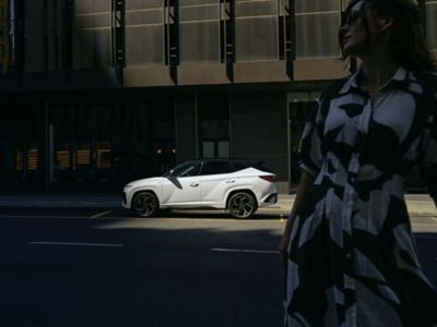 Hyundai TUCSON parcheggiata su una strada cittadina, con una donna in piedi ritratta di fronte al veicolo 