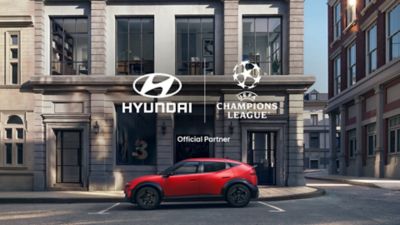 Red Hyundai IONIQ 3 parked in front of Hyundai and UEFA Champions League branding as part of Hyundai's Official Partner sponsorship.