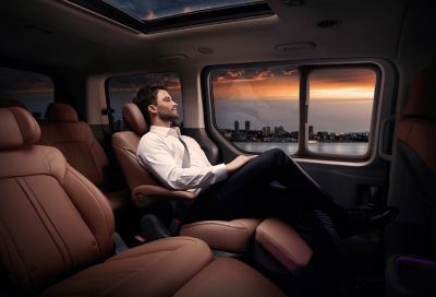 Een man zit op een van de comfortabele achterzetels in de volledig nieuwe Hyundai STARIA Premium.