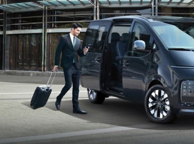 A business man checking his phone, going towards the all-new Hyundai Staria Premium.