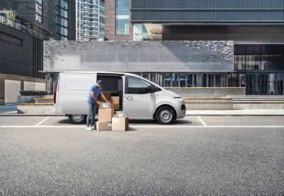 The STARIA Hybrid Van parked next to a modern building.