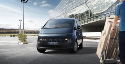 Hyundai STARIA Hybrid Van vue de côté devant un bâtiment futuriste.