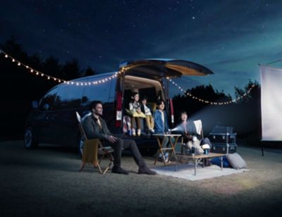 Familia viendo una película en un camping junto al nuevo Hyundai STARIA. 