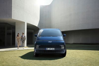 Vooraanzicht van de volledig nieuwe Hyundai STARIA die geparkeerd staat op een stuk openbaar groen.