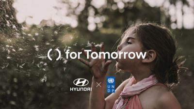 Immagine di bambina immersa nella natura che soffia petali con slogan Hyundai for Tomorrow