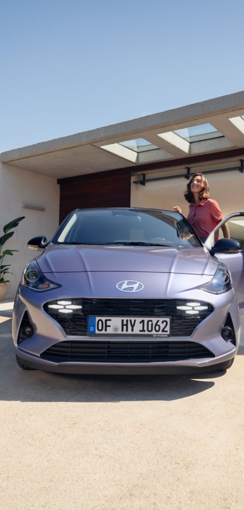 Hyundai i30 seen from rear three-quarter driving on a city street in front of modern buildings.