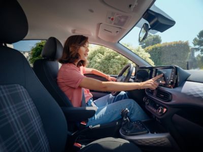 Una donna che utilizza il pannello touch screen mentre guida Hyundai i10.