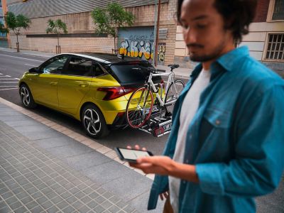 A man standing next to a Hyundai i20 with a trailer hitch mounted bike rack with a bike on it. 