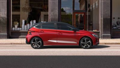 Hyundai i20 rouge garée dans les rues avec son accessoire de bandes sportives captivantes.