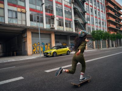 Une femme faisant du skateboard dans les rues avec Hyundai i20 en arrière-plan.