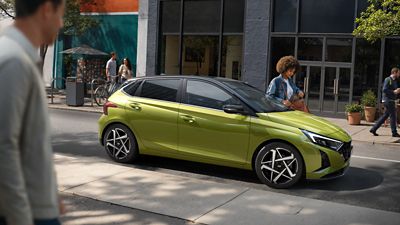 Hyundai i20 parked on a city street as a person walks nearby.