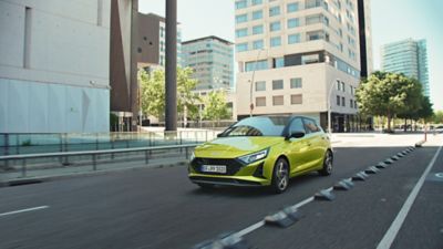 Der Hyundai i20 in der aufpreispflichtigen Farbe Lucid Lime Metallic fährt auf einer innerstädtische Straße.