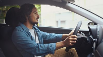 Un homme en chemise bleue, les mains sur le volant conduisant la nouvelle Hyundai i20.