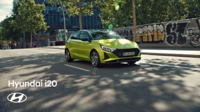 Ein Hyundai i20 in der aufpreispflichtigen Farbe Lucid Lime Metallic fährt auf einer von Bäumen beschatteten Straße.