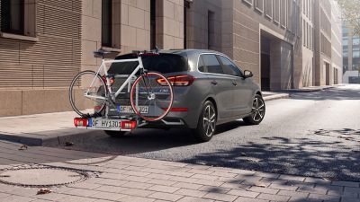 The i30 Hatchback with a rear mounted bike carrier by Hyundai Genuine Accessories parked in front of a building. 