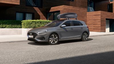 The i30 Hatchback parked in front of a big house with a roof box from Hyundai Genuine accessories. 