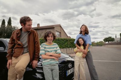 A family of four leaning on or standing near the front of the new Hyundai i30.