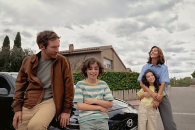 Šťastná štvorčlenná rodina opierajúca sa alebo stojaca v blízkosti prednej časti nového Hyundai i30.