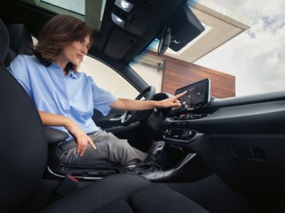 Une femme assise sur le siège du conducteur, utilisant l'écran tactile multimédia sur le tableau de bord.