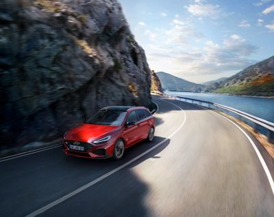 Der rote i30 Wagon N Line in Fahrt auf einer kurvigen Strecke.zwischen Felswand und Gewässer.