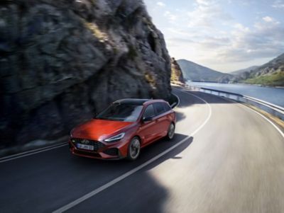 Der rote i30 Wagon N Line in Fahrt auf einer kurvigen Strecke.zwischen Felswand und Gewässer.