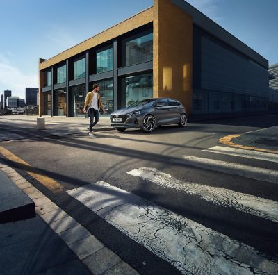A man standing next to the Hyundai i20 in front of a building with large windows