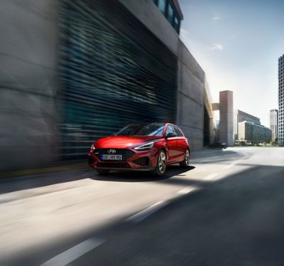 De Hyundai i30 N Line in het rood rijdt door een stad voor een gebouw. 