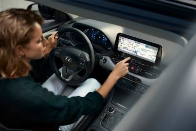 Mujer controlando la pantalla táctil de su Hyundai i30 desde el asiento del conductor.