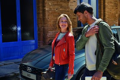 A woman and a man talking to each other next to the Hyundai i20, front left view