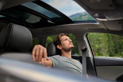 Man kijkt ontspannen door geopend panoramisch zonnedak van zijn geparkeerde Hyundai i30 Wagon.