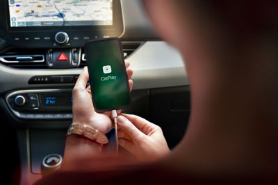 A Hyundai driver in an i30 holding an iPhone with the Apple CarPlay logo in the phone display.