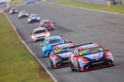 Hyundai N racing cars compete on a track, leading a line of vehicles during a motorsport event.