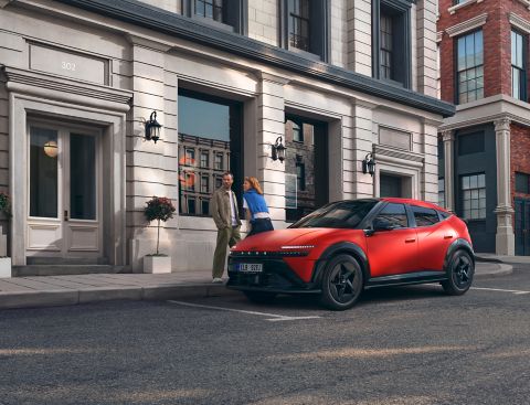 Muž a žena stojící vedle červeného Hyundai IONIQ 3 zaparkovaného v městské ulici.