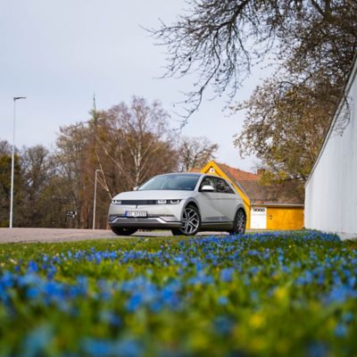 IONIQ 5 parkert ved ett hvitt gjerde med blå blomster. Foto.
