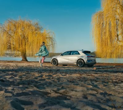 Ragazza corre vicino a IONIQ 5 su spiaggia