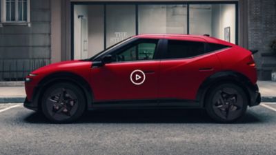 Red Hyundai IONIQ 3 driving on an urban road, shown from a front three‑quarter angle.