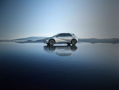 A surfer approaching her Hyundai IONIQ 5 electric vehicle parked on the beach.