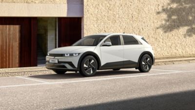 Zijaanzicht Hyundai IONIQ 5 Pure Edition geparkeerd voor gebouw.