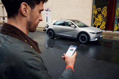 Ragazzo ricarica IONIQ 5 e guarda telefono con schermata Bluelink