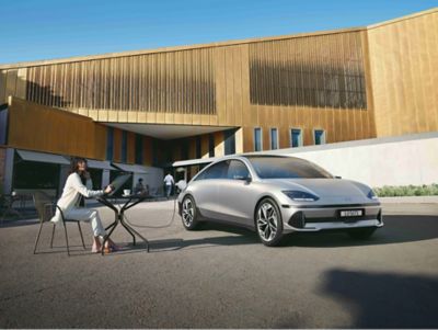 A lady charging a laptop via the exterior charging port of the Vehicle-to-Load technology of IONIQ 6.