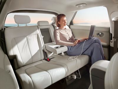 A women in back of Hyundai IONIQ 5 electric CUV working using V2L to charge laptop.