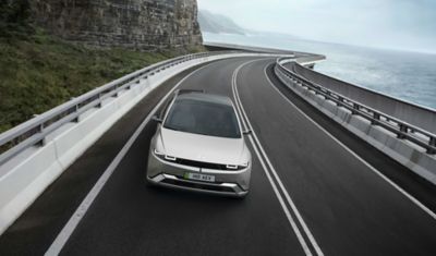 Front view of new Hyundai IONIQ 5 in grey driving along a curving seaside road.