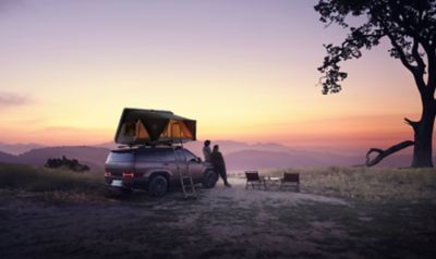 Due persone appoggiate a Hyundai SANTA FE che ammirano il tramonto dall’alto di una montagna