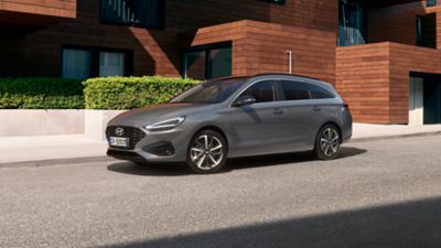 Vista a tre quarti di nuova Hyundai i30 Wagon di colore grigio, parcheggiata di fronte a un’abitazione in stile moderno