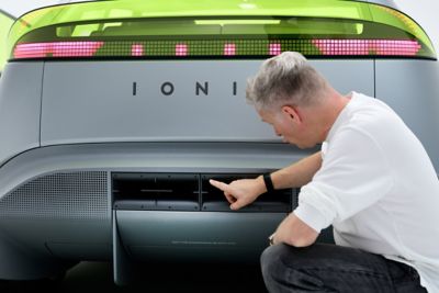 Persoon gehurkt bij achterzijde Hyundai Concept THREE en wijzend naar diffusor.