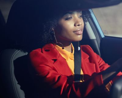 A woman sitting behind the wheel of her Hyundai KONA, looking very relaxed.