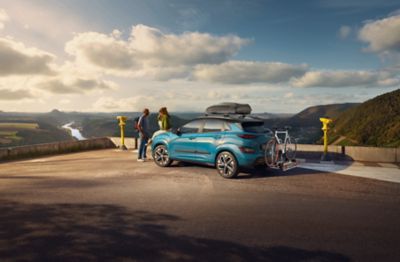 Hyundai KONA Electric z bagażnikiem rowerowym montowanym na hak holowniczy oraz  boksem dachowym.