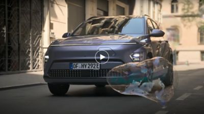 The Hyundai KONA Electric driving on the street while a soap bubble is passing.