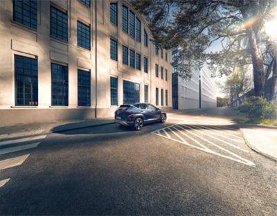 A woman crosses the street with a green Hyundai KONA is parked on the other side. 