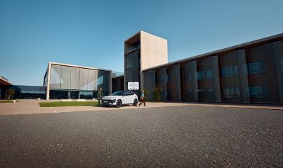 The man opening the door of the all-new Hyundai KONA in green parked in front a building. 